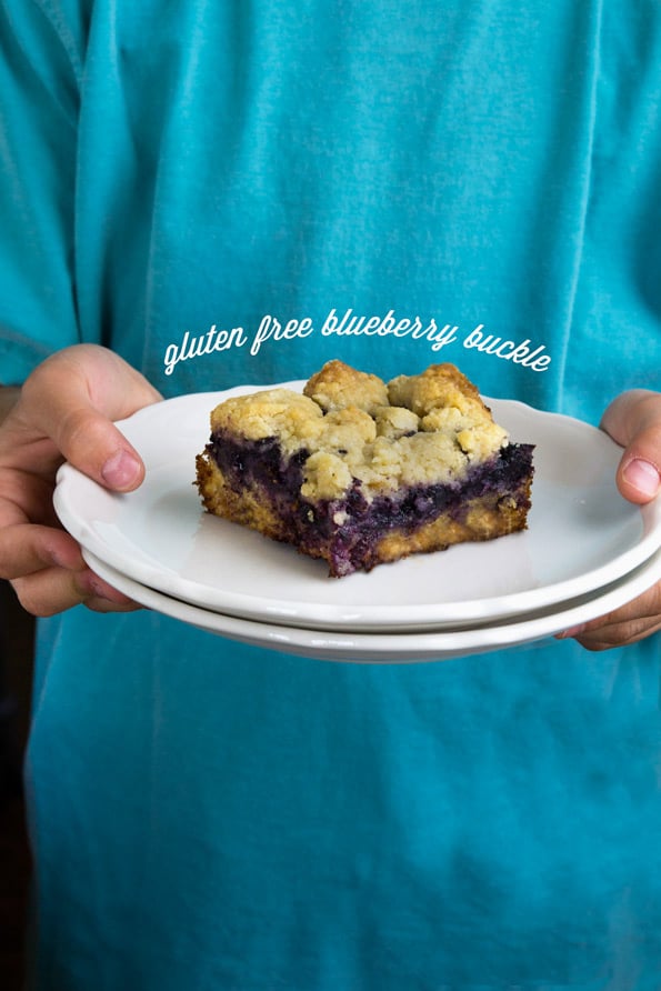 A person holding a piece of blueberry buckle on a white plate