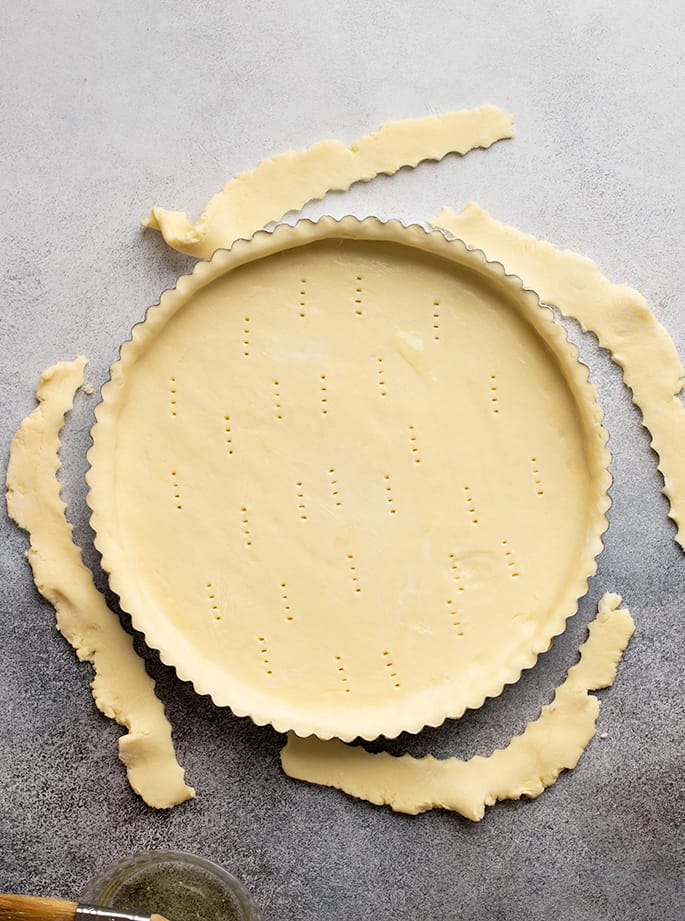 Overhead image of raw tart crust in pan with scraps on sides of pan