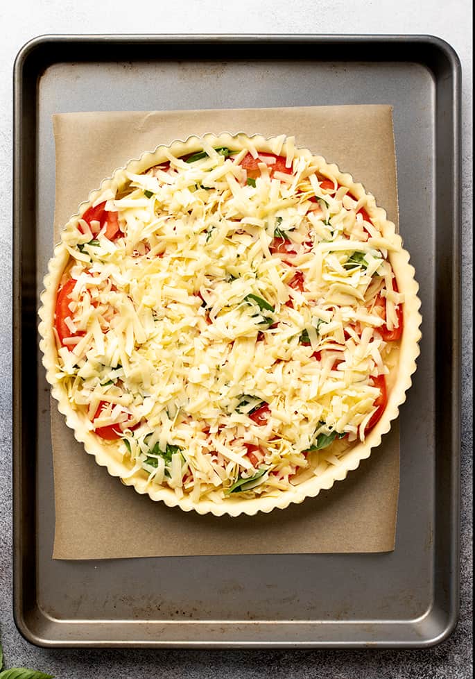 Overhead image of unbaked tomato tart on brown paper on metal baking sheet