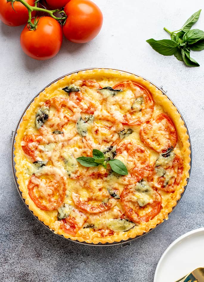 Overhead image of whole baked tomato tart with whole tomatoes and basil leaves