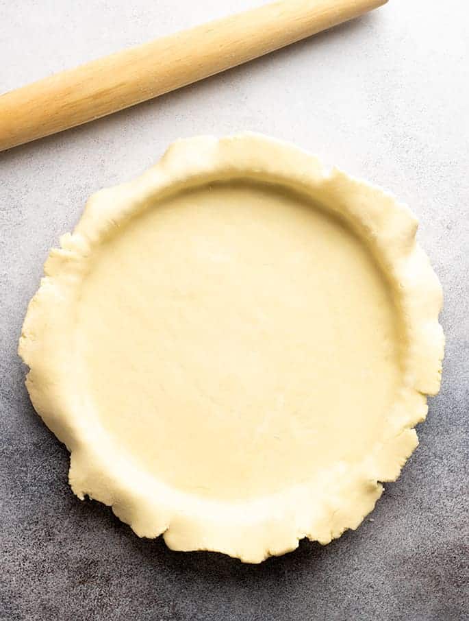 Raw savory tart crust draped over round tart pan with rolling pin on gray surface