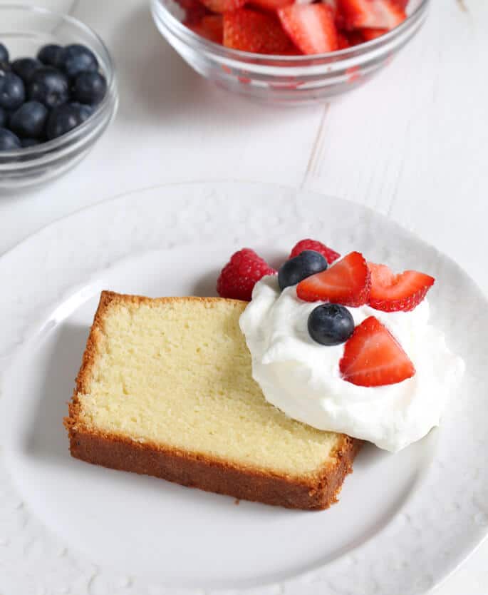 A close up of pound cake with whip cream and fruit on white plate 