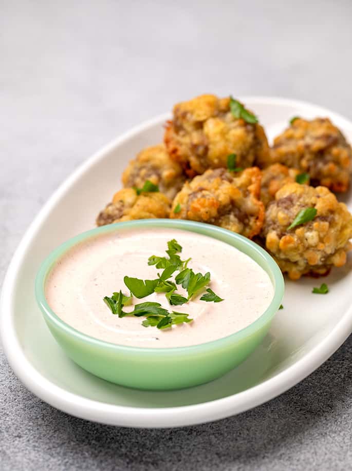 Light orange dipping sauce with fresh parsley in small green bowl with sausage balls on platter