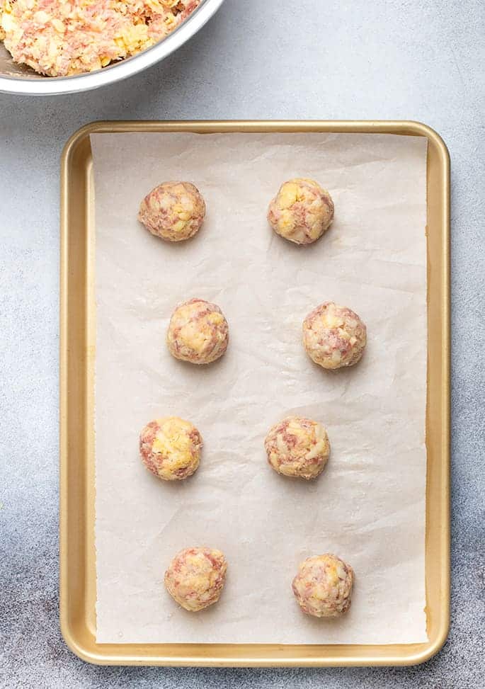 Overhead image of raw sausage balls on white paper on gold baking tray