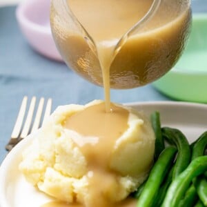 Small square image of gravy boat pouring gravy onto mashed potatoes with string beans on white plate