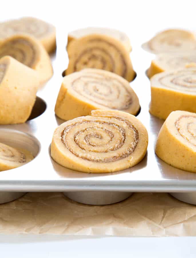 raw shaped pumpkin cinnamon rolls in metal muffin tray 