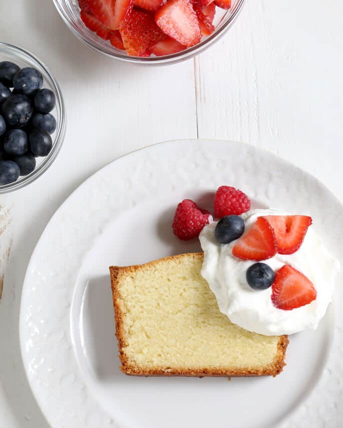 Overhead view of gluten free pound cake, whip cream and fruit on a white plate