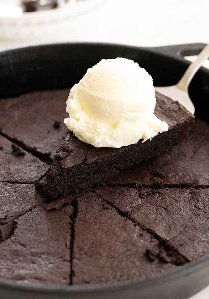 Skillet brownie slice on a spatula with a scoop of vanilla ice cream