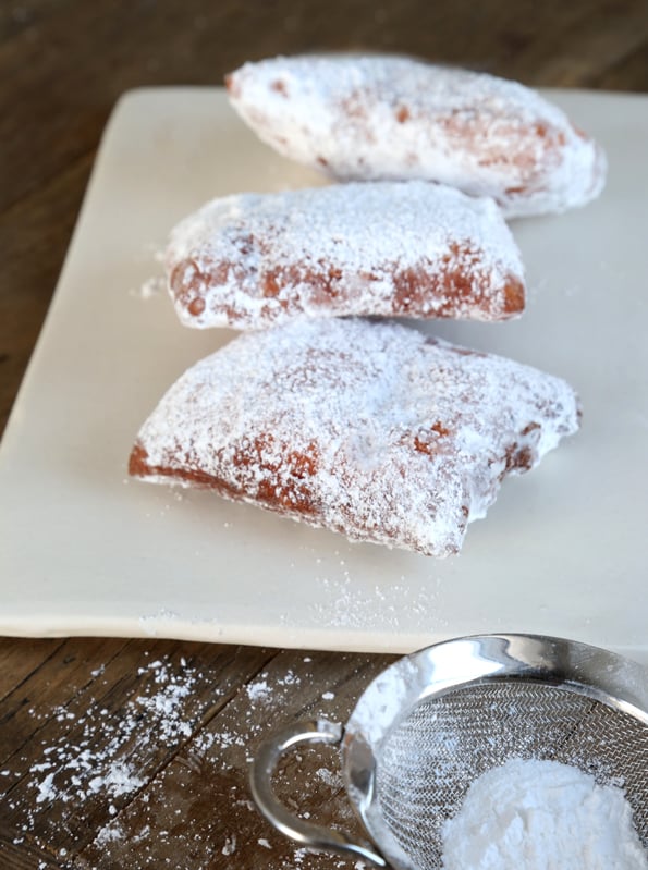 Close up of gluten free beignets coated with powdered sugar on white surface 