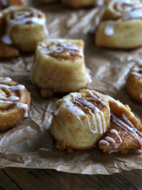 Cinnamon roll sugar cookies drizzled with icing, unfurling on a tray