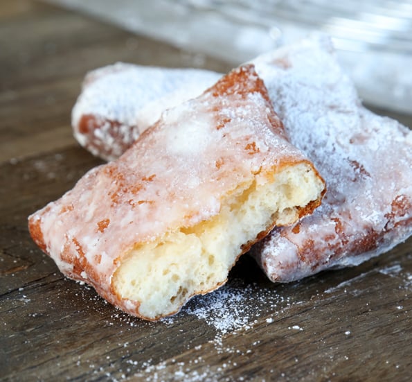 A close up of gluten free Beignets coated with powdered sugar on wooden surface 