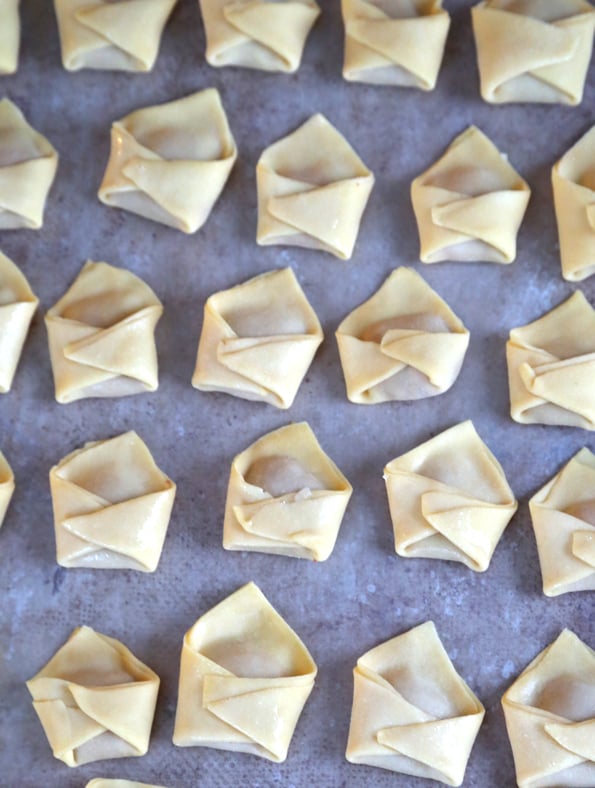 Overhead view of raw filled and shaped wontons on wax paper on table