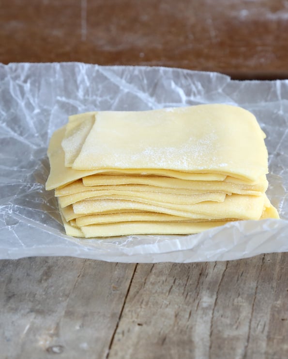 stack of shaped and cut wonton dough on wrinkled wax paper on wooden surface 