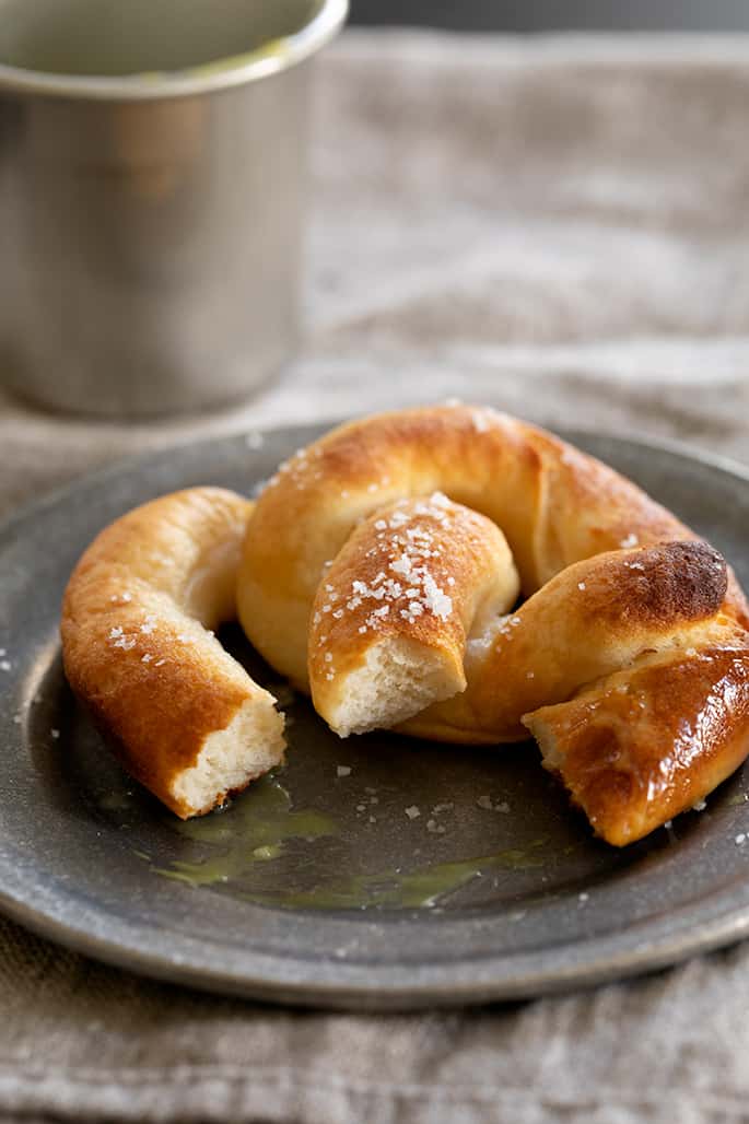 A partially eaten gluten free soft pretzel on a plate with dipping sauce.