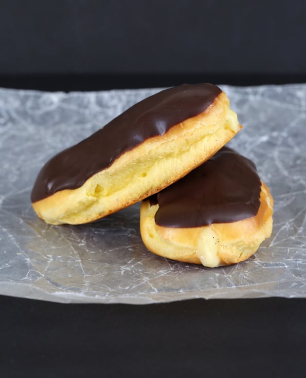 chocolate eclairs leaning against each other on a white surface 