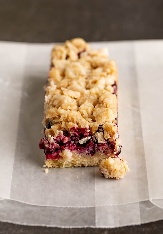 Side image of blueberry breakfast bar with crumble topping falling off sitting on wax paper bag