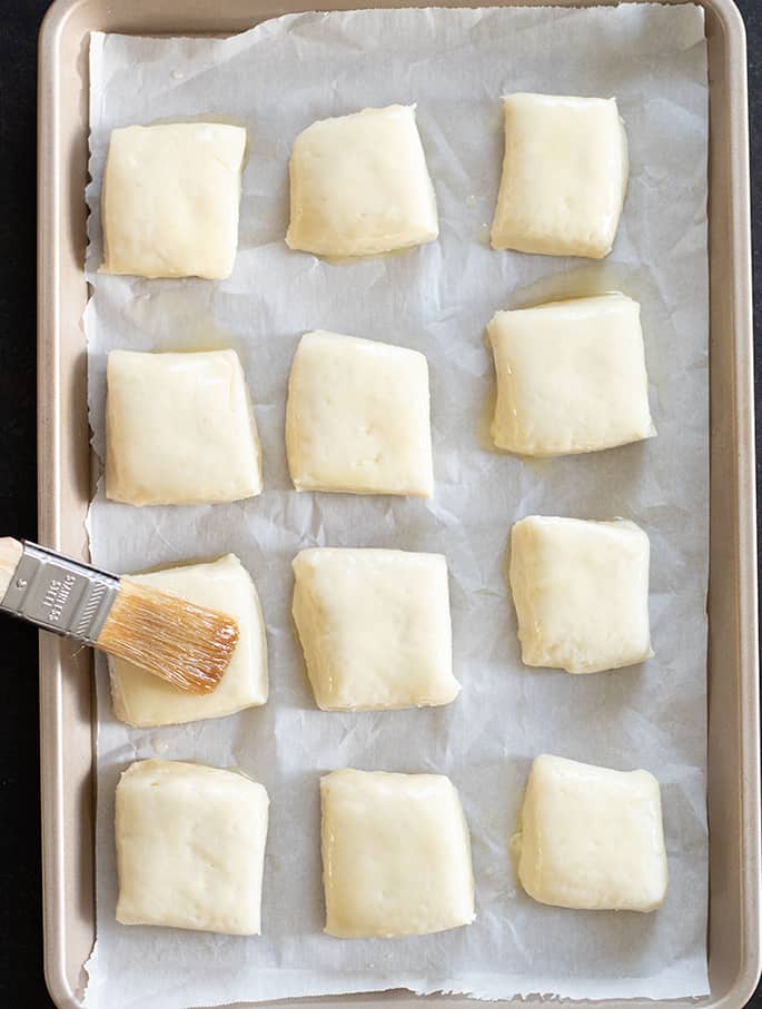 Gluten free Texas roadhouse rolls raw risen being brushed with honey butter before going into the oven.