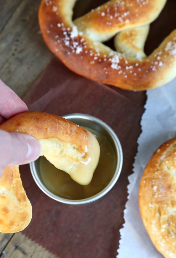 A close up a broken gluten free soft pretzel being dipped in sauce.