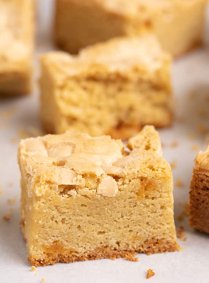 Closeup image of square gluten free blondies on white paper with more blondies in background