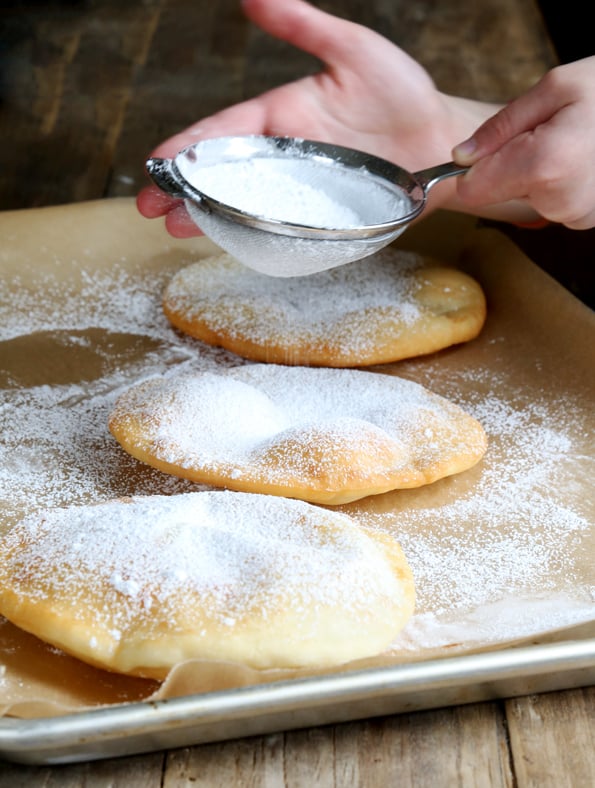 Fry bread with powdered sugar being sifted on top on metal tray