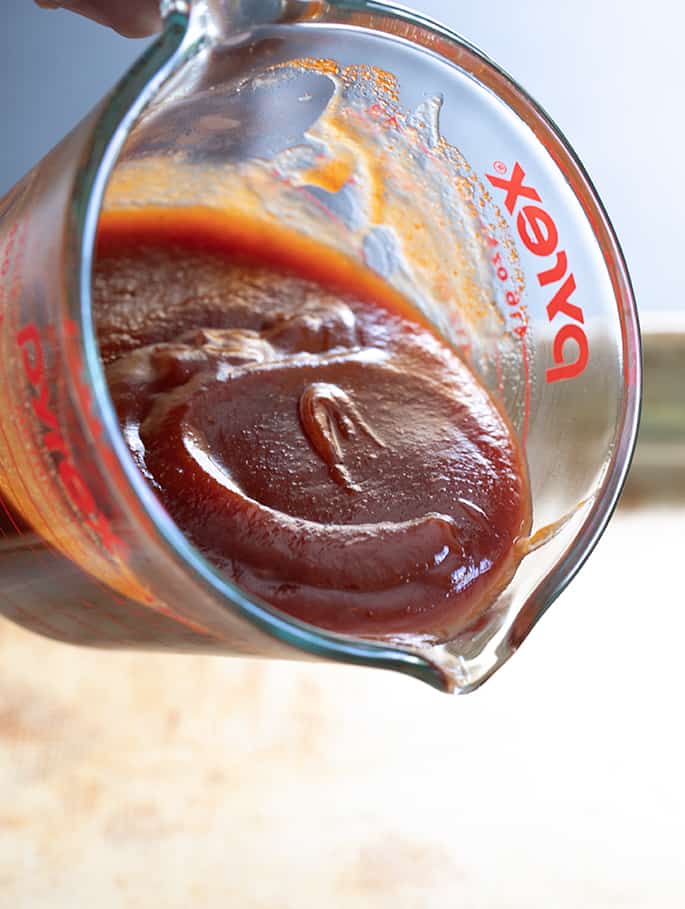 Homemade BBQ sauce being poured out of a measuring cup