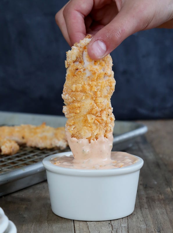 Gluten Free Crispy Buttermilk Coconut Chicken Fingers Chicken finger being dipped in sauce