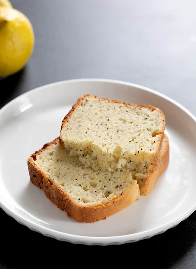 Two slices of gluten free lemon poppyseed bread on a plate, one broken in half to show moist and tender crumb inside.