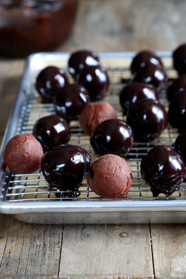 Chocolate donut holes on metal tray with glaze being put on donuts