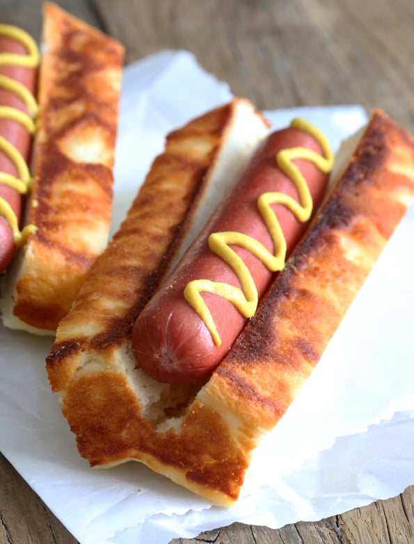 A close up of New England Hot Dog Buns with hot dog and mustard inside on white surface 