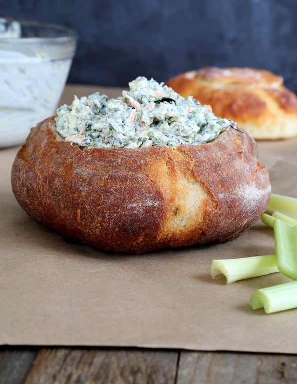 A close up of spinach dip in a bread bowl on brown surface 