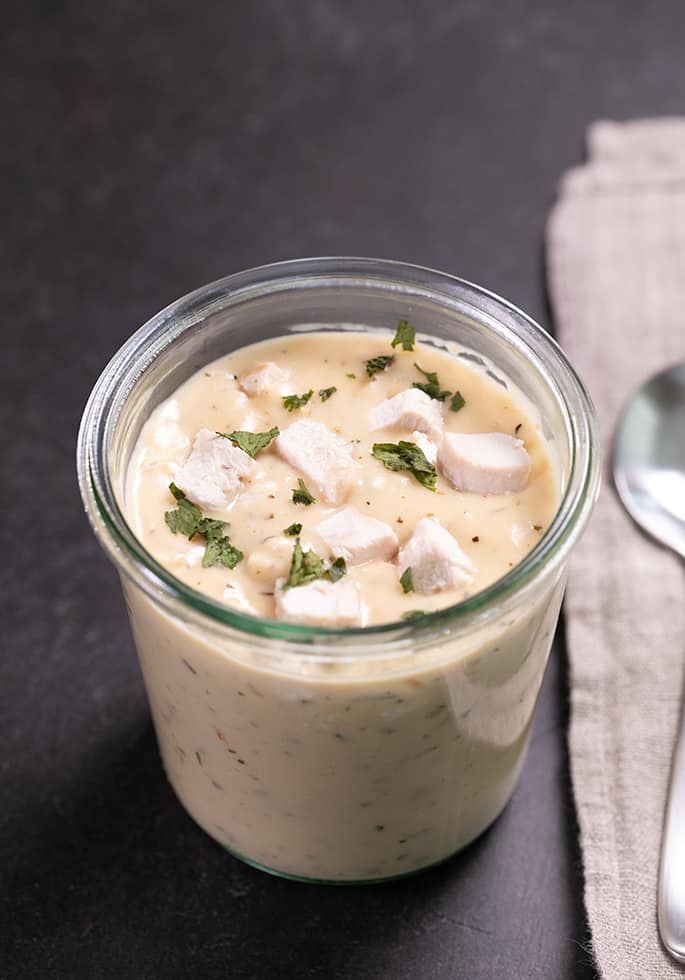 Cream of chicken soup in a glass jar with parsley pieces on top and a clean spoon on a cloth