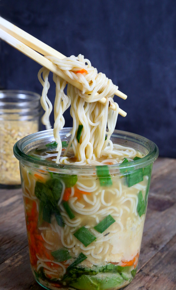 A close up of a mason jar of soup, with chopsticks and noodles.