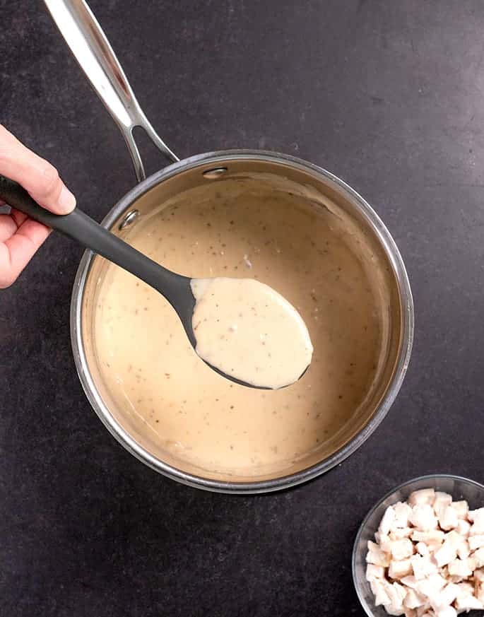 Overhead image of spoonful of cream of chicken soup in black spoon over pan