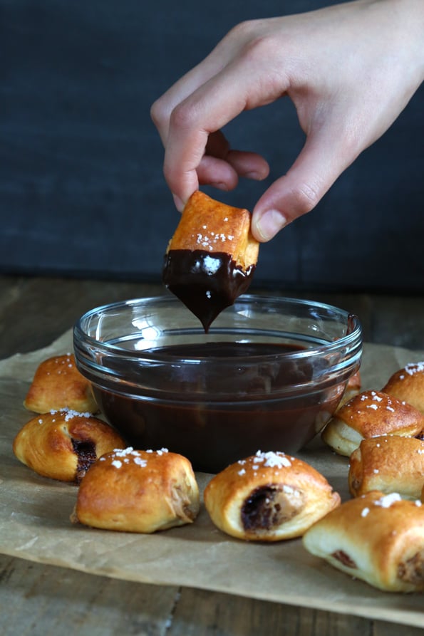 Person holding pretzel bite with chocolate sauce on it over bowl of chocolate sauce 