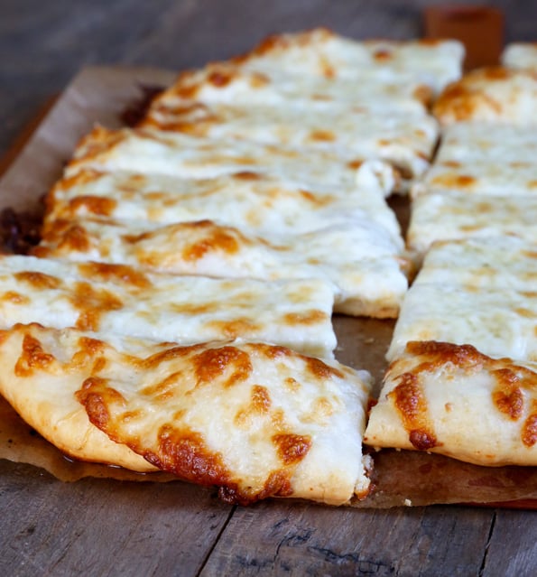 A slice of pizza sitting on top of a wooden cutting board cut into breadsticks