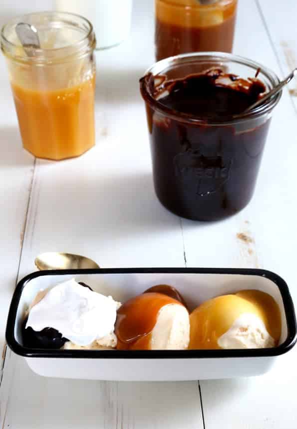 rectangular white dish with three scoops of ice cream with brown, orange and yellow sauces, brown sauce in a jar, yellow sauce in a jar on white table