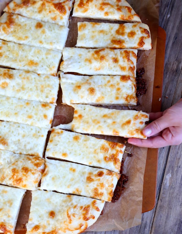 Garlic breadsticks pictured from above with a hand taking one