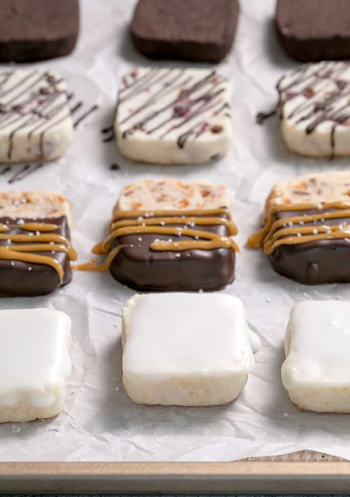 Lemon glazed, toffee caramel, berry chip, and mocha shortbread cookies on white paper on a tray