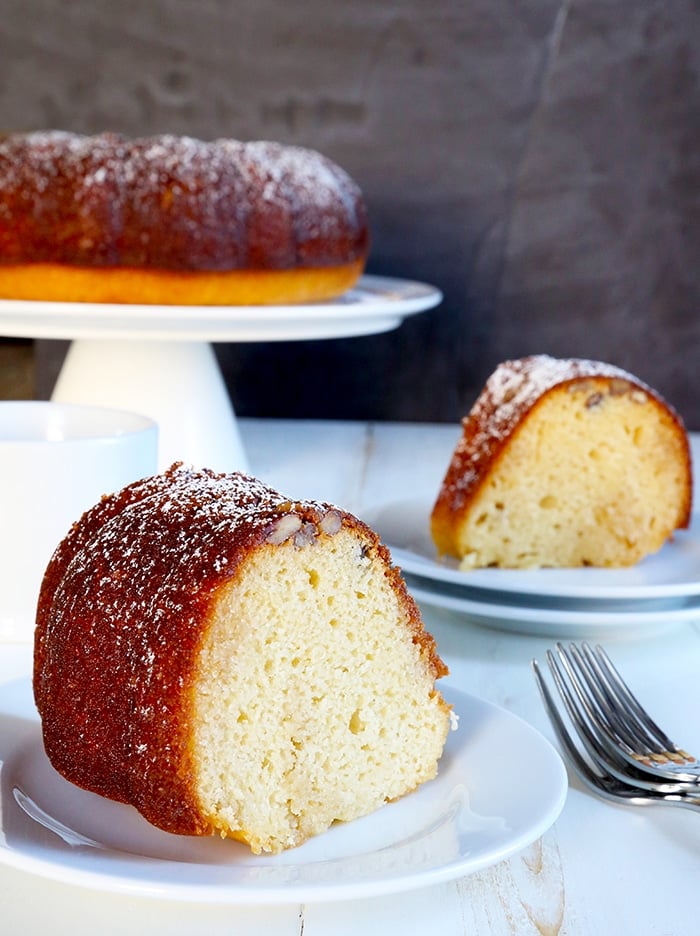 Two slices of rum cake on white dessert plates with rest of rum cake on serving platter in background