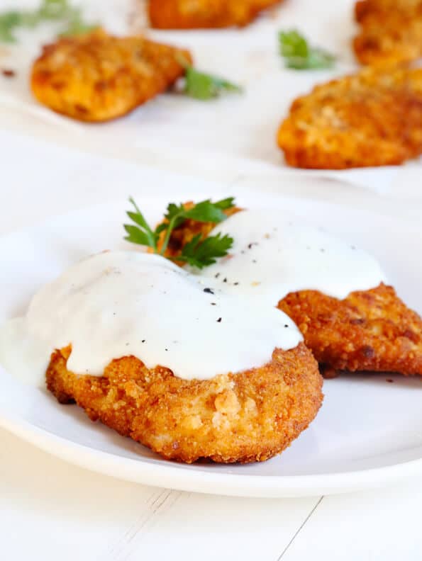 Fried chicken with white sauce and herbs on a white plate