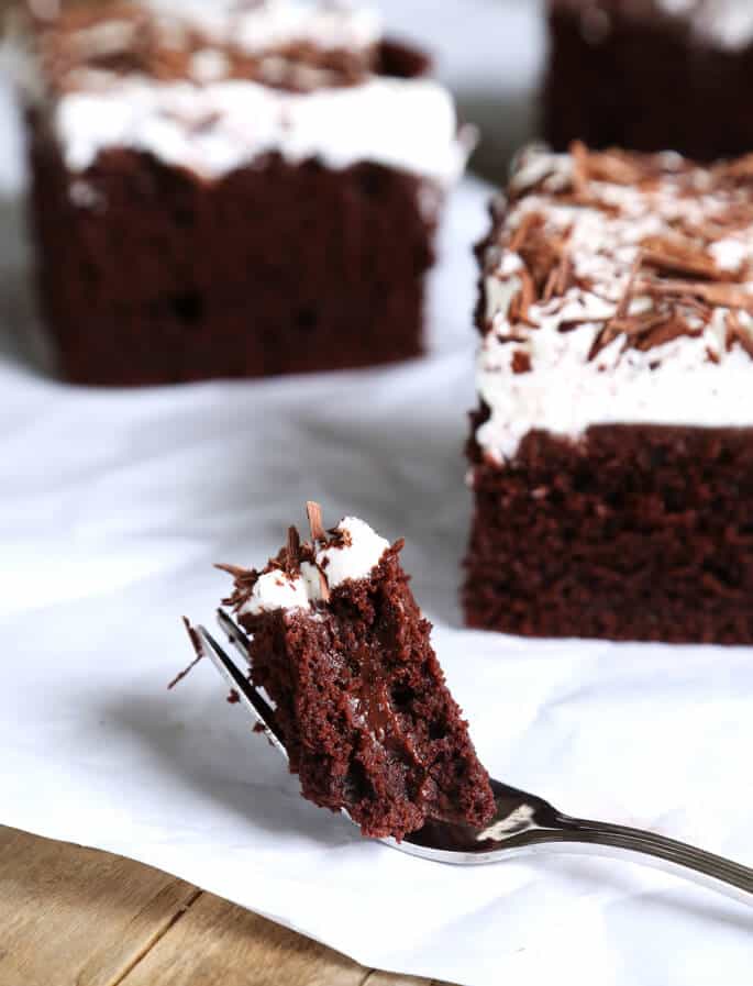 A close up of a bite of chocolate poke cake on a from on white surface 