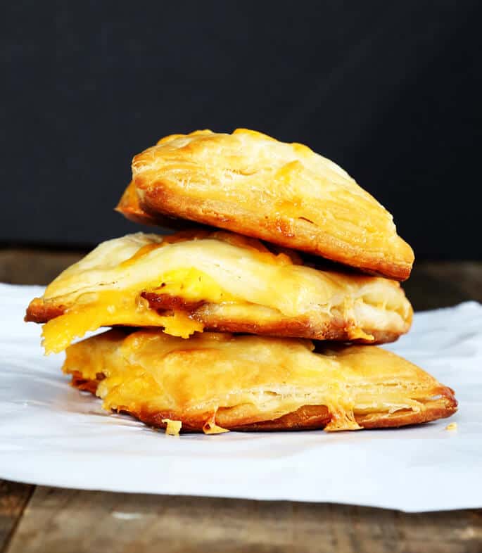 A stack of 3 bacon egg and cheese biscuits on a white surface 