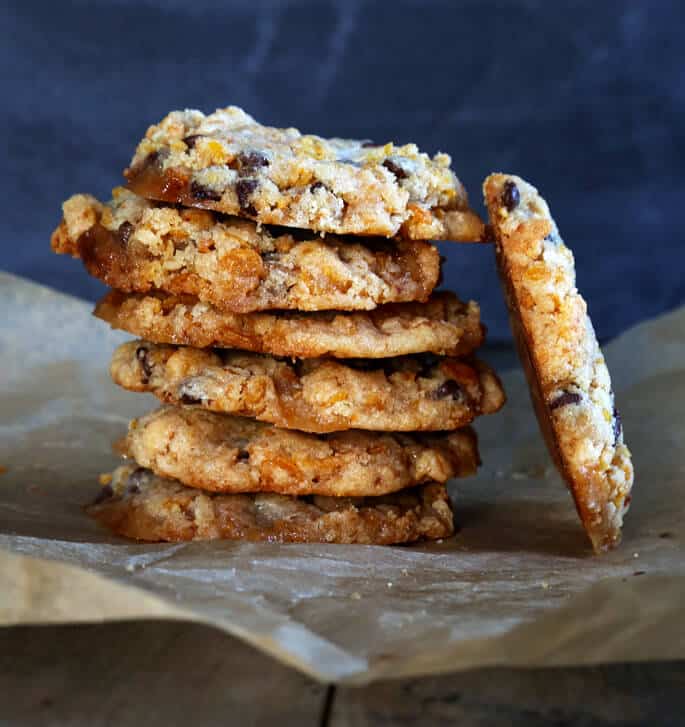 A stack of chocolate chip marshmallow cookies with one leaning on side of stack on brown surface 