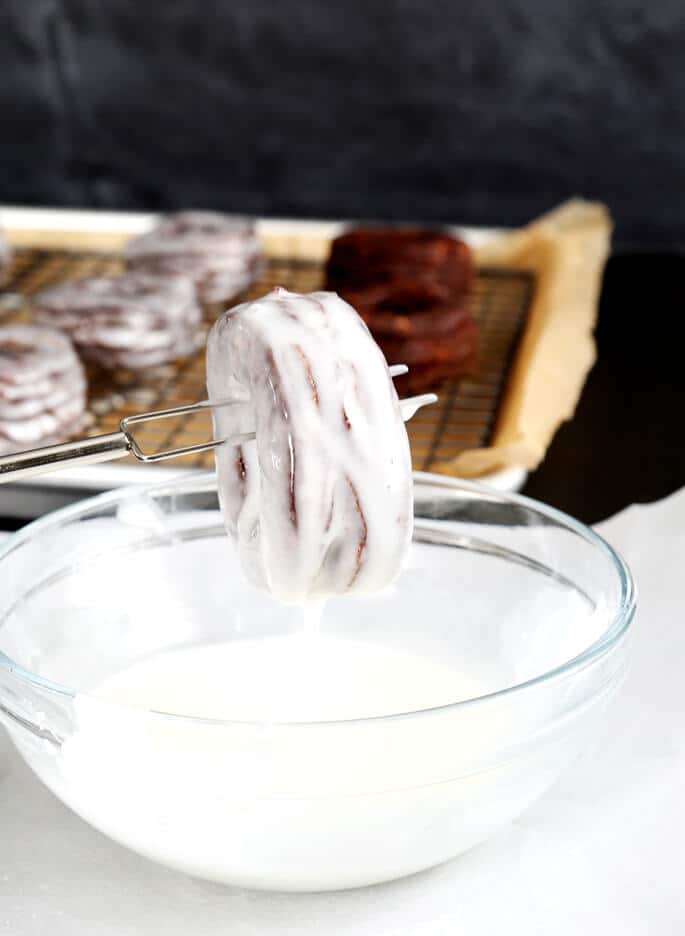 Chocolate donut being dipped in bowl of glaze