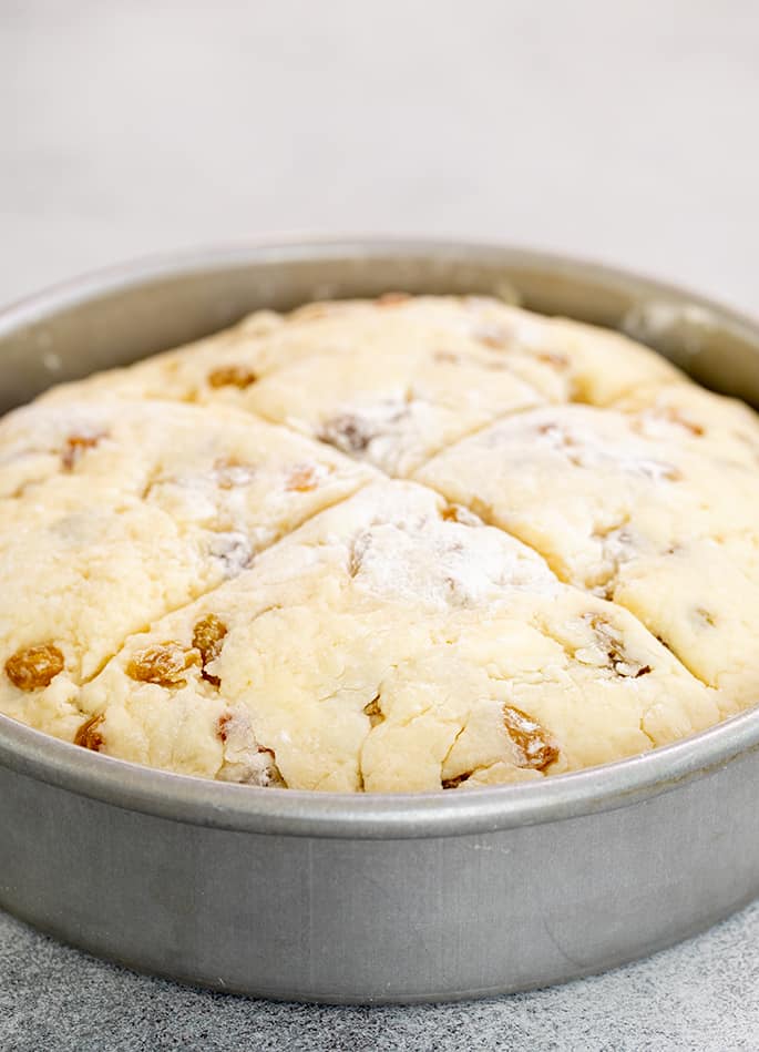 Closeup of shaped raw bread dough with raisins in round metal baking pan