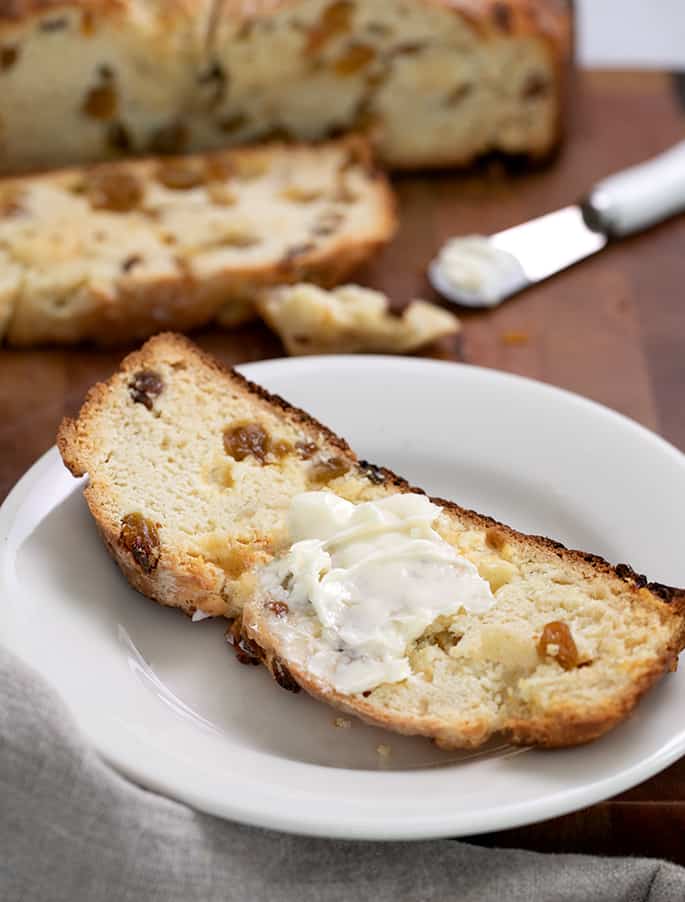 narrow, long bread slice with raisins and softened butter on top on small white plate