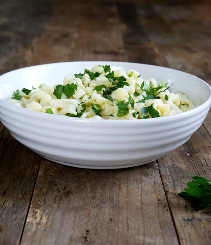 A white bowl with gluten free spaetzle and herbs