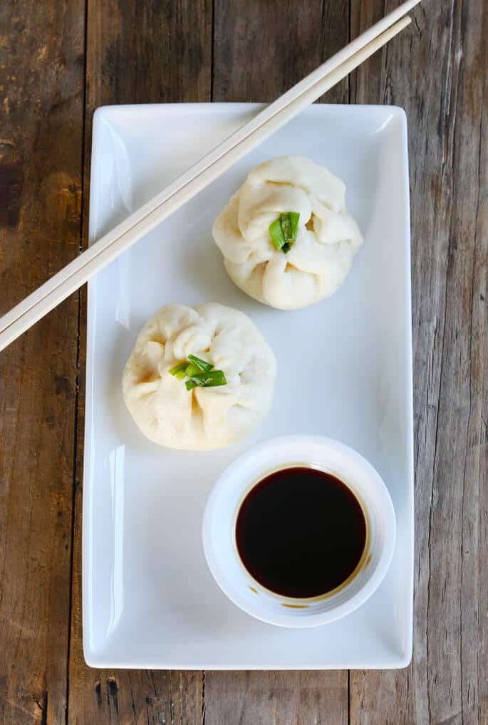 Overhead view of a white plate with 2 Chinese meat buns and soy sauce 