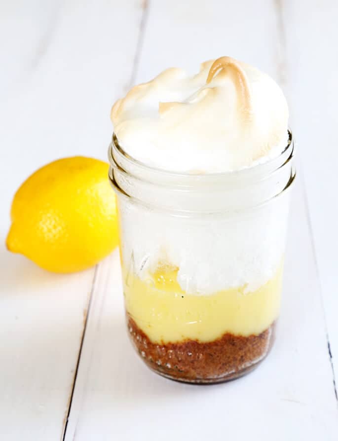 A close up of lemon meringue pie in a jar on a white surface