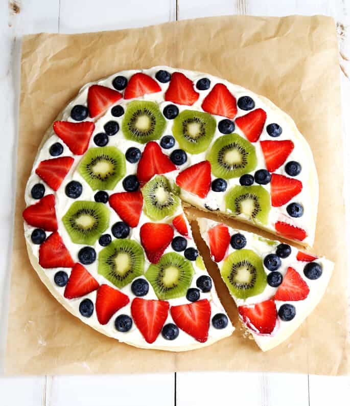 Overhead view off a fruit pizza on beige paper